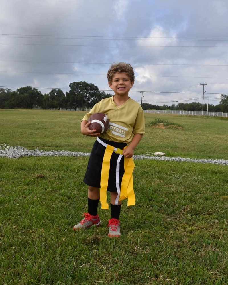 Young boy holding and running with a football during a flag football game