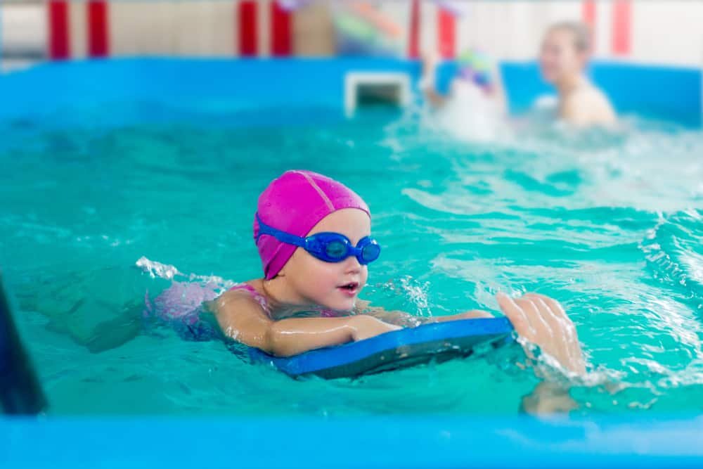 child in a pink rubber hat and blue glasses is swimming in a pool