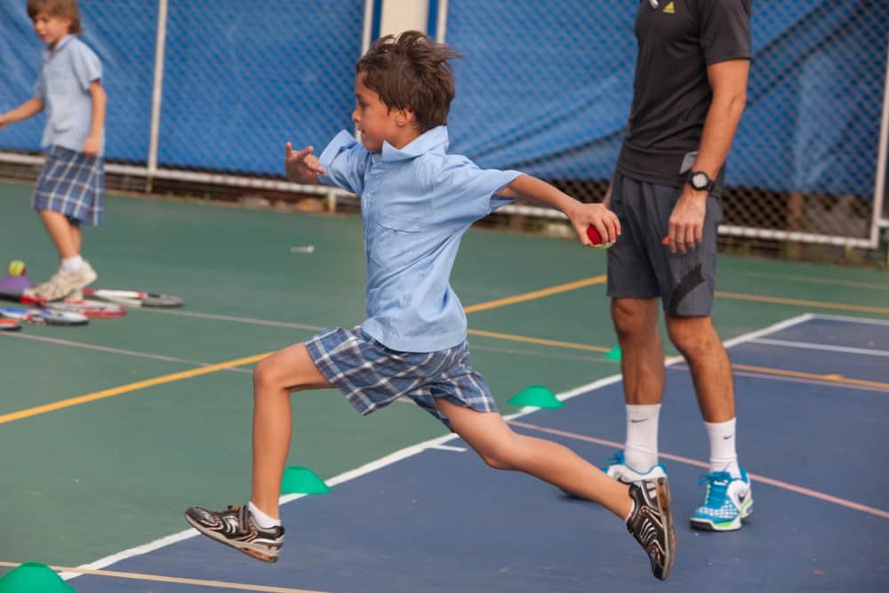 school children take an outdoor tennis lesson