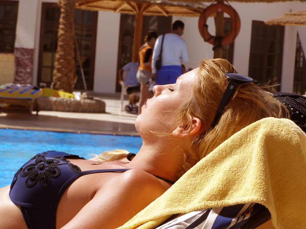 woman lies on a sun lounger with her eyes closed by the pool and tans