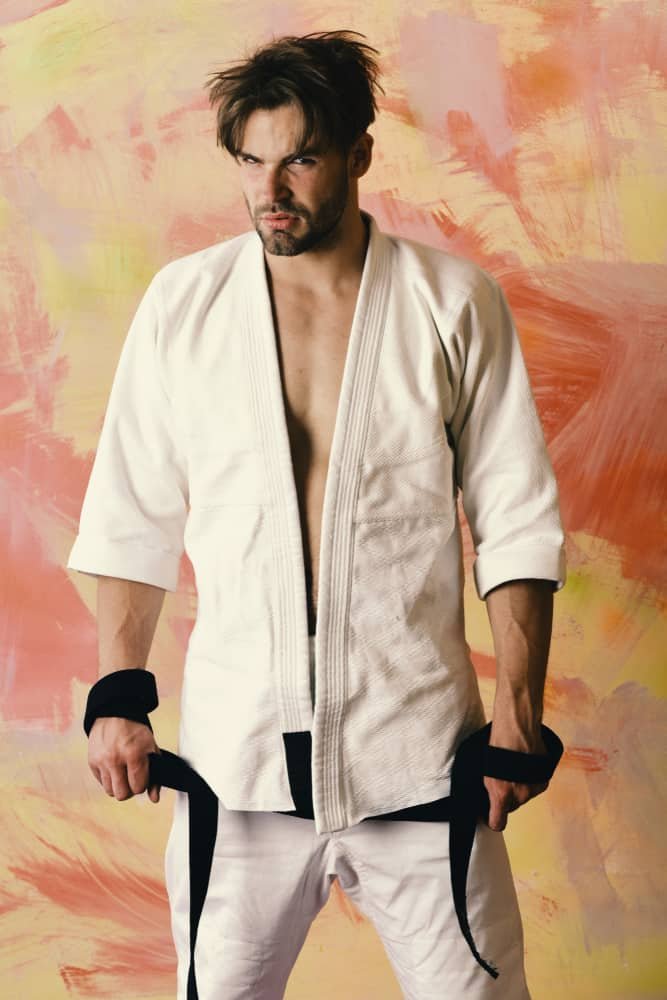 Guy poses in white kimono holding black belt taekwondo